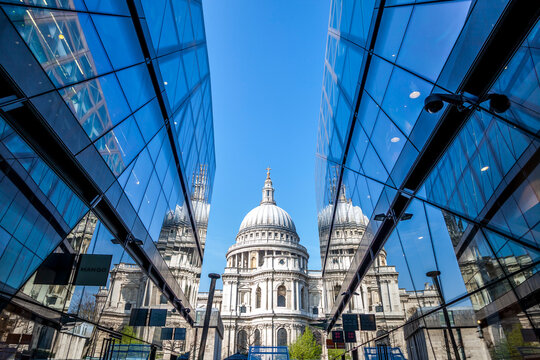 St paul's cathedral's dome reflecting in the glass facade of one new change against a blue sky