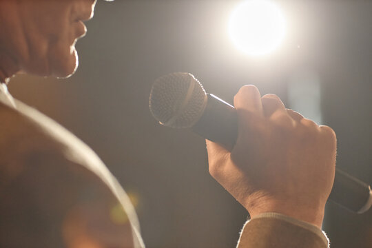 Close up of middle aged speaker holding microphone and performing standup on stage, conveying public speaking and live entertainment. Useful for event promotion, comedy marketing, speaker branding
