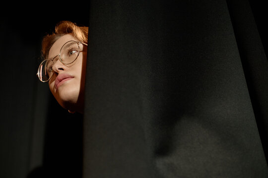 Close up of Caucasian young woman peeking from stage curtain, preparing for standup performance and live presentation. Supporting comedy promotion, event marketing, entertainment ads
