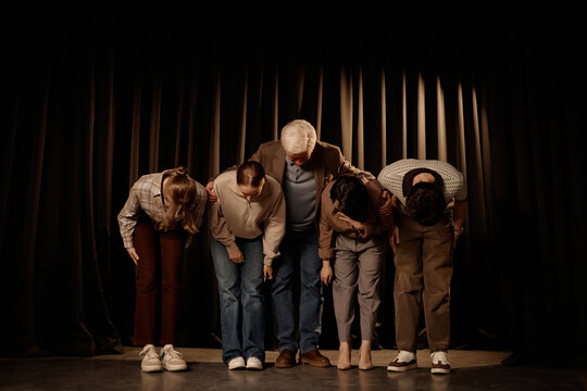 Wide shot of diverse adult comedy team bowing on stage after standup performance, signaling live entertainment success. Useful for event promotion, theater marketing, ticket sales

