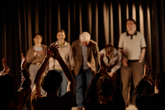Wide shot of diverse adult comedians taking bow on stage during standup performance while audience clapping, conveying live entertainment and event success. Useful for comedy promotion and ticket mark