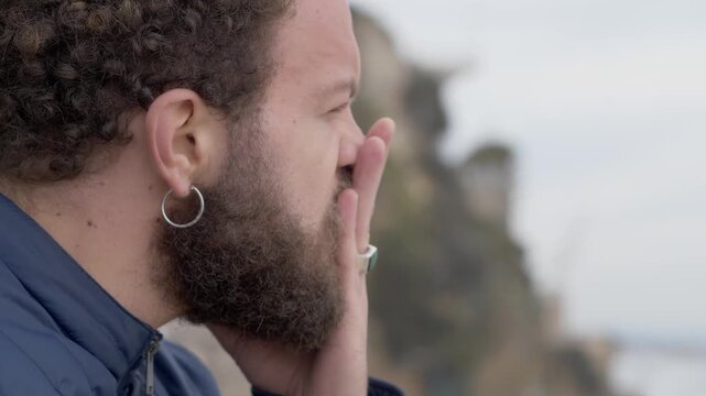 Young brown haired man in profile by the sea first sad then looking at camera angrily. Emotional scene showing change of mood and inner conflict.