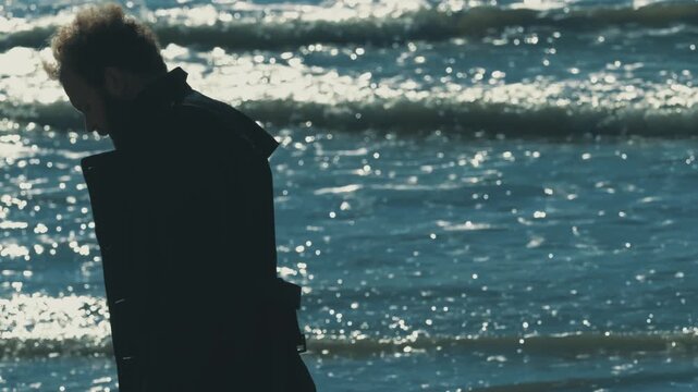 Young brown haired man seen from behind looking at the sea visibly shaken. Emotional outdoor scene expressing stress, confusion and inner turmoil.