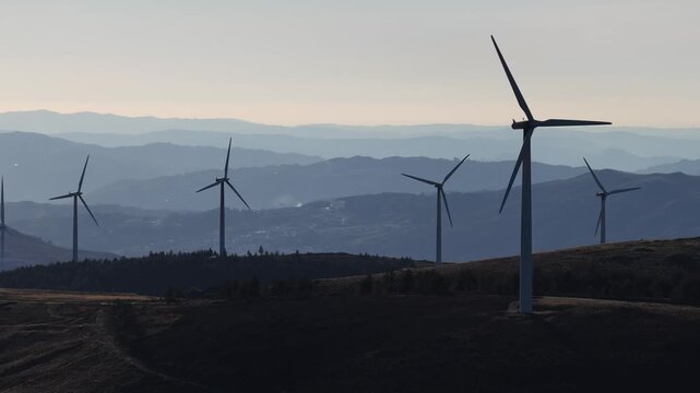 Aerial view of wind turbines against a hazy mountain backdrop, creating a layered effect of blues and greens, Amarante, Portugal.