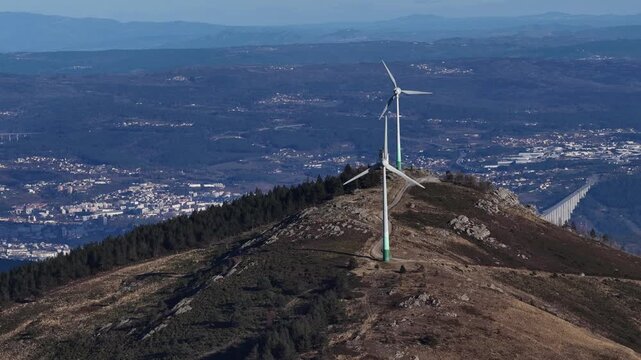 Aerial view of wind turbines on a mountain with a long bridge spanning across the landscape in the background, Amarante, Portugal.