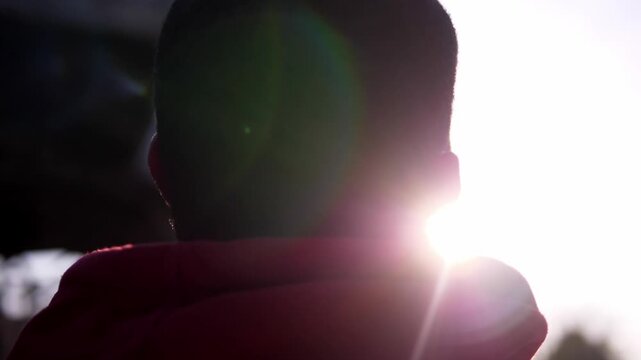 Young African American man in a red hoodie looks at the sky reflecting on his past and imagining a better future. The scene expresses hope, dreams, and personal growth.