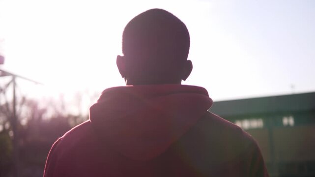 Rear view of a young African American man in a red hoodie looking at the sky. The scene expresses determination, hope, and a desire to move forward in life.