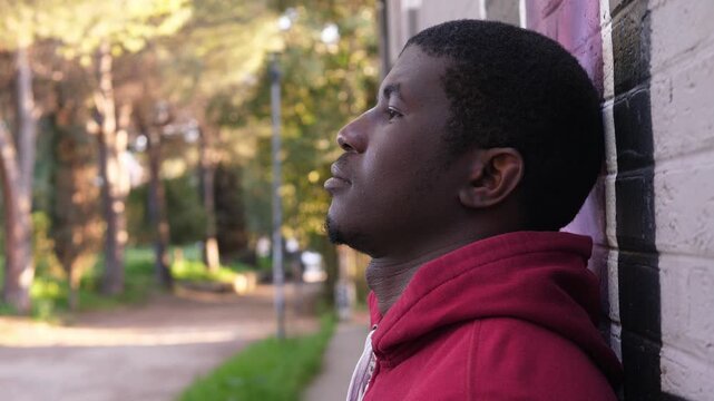 Side view of a young African American man in a red hoodie looking down with a defeated expression. The scene conveys regret, sadness, and emotional weight.