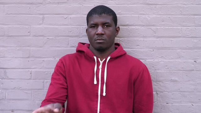 Young African American man in a red hoodie gestures no with his fingers, expressing disagreement and refusal. The scene communicates a clear negative response.