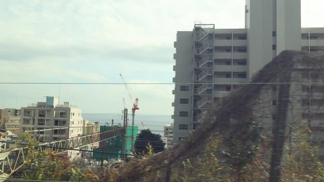 A view of a coastal city with buildings and the ocean from a moving train in japan, dynamic footage captures urban landscape and sea.