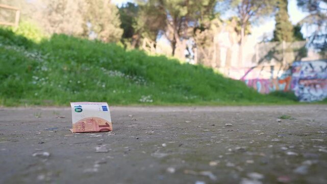 Ten euro banknote lies on the ground, forgotten and unnoticed. The scene conveys themes of loss, chance, and overlooked value in a simple everyday outdoor setting.