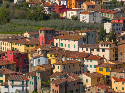 Aerial view of the historic center with colorful houses, terracotta rooftops, and a prominent red clock tower surrounded by olive groves in Loro Ciuffenna, Tuscany, Italy.