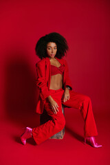 Fototapeta premium Fashionable young woman confidently poses in bold red attire against a vivid backdrop