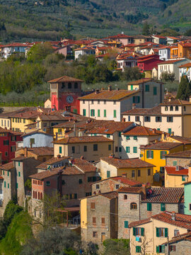 Aerial view of the historic town center with colorful houses, terracotta tiled roofs, and a prominent clock tower nestled against green hills in Loro Ciuffenna, Tuscany, Italy.