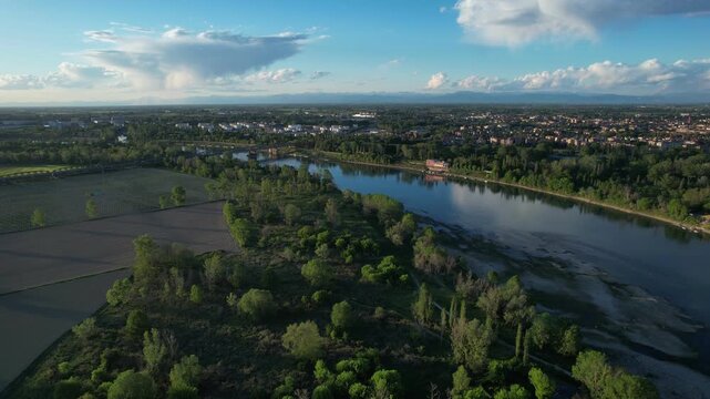 Po River flowing through countryside in Castelvetro Piacentino, Cremona, Lombardy Italy accross, with agricultural fields, riverside vegetation and distant iron bridge spanning drone ascending