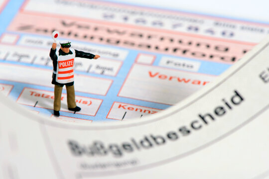 Ein Modell-Polizist steht auf einem Bu&szlig;geldbescheid und Verwarnungszettel