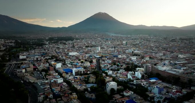 Wide drone view of the cityscape of Arequipa, the white city, with the Misti volcano in silhouette at sunrise, Peru. Aerial forward