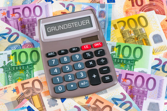 Ein Taschenrechner steht auf vielen Euroscheinen und im Display erscheint das Wort Grundsteuer - FOTOMONTAGE