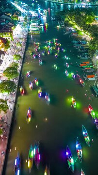 Aerial hyperlapse sequence of colorful lantern boats moving along the Thu Bon River past crowds of tourists in the ancient town of Hoi An, Vietnam.