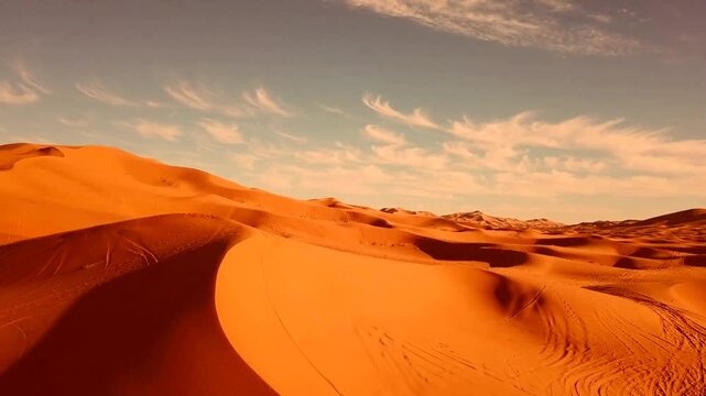 A breathtaking aerial view of the Sahara Desert, showcasing vibrant orange sand dunes under a serene, cloud-dotted sky. Footprints create intriguing patterns across the landscape.