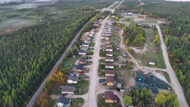 High aerial drone shot over War Lake Ilford First Nation in northern Manitoba. Community along train tracks to Churchill with houses, roads, and misty boreal forest in early morning light.