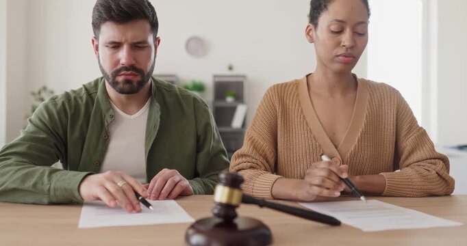 Couple signing divorce agreement legal contract document. Spouses sit with pens near gavel, reviewing files before court under law and discussing custody. Strong concept of legal separation process.