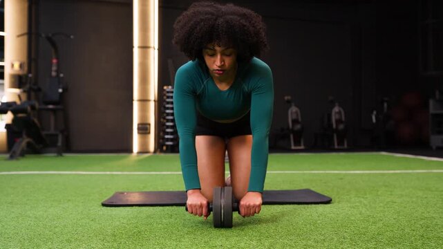 Focused african american woman performing ab roller exercise at the gym