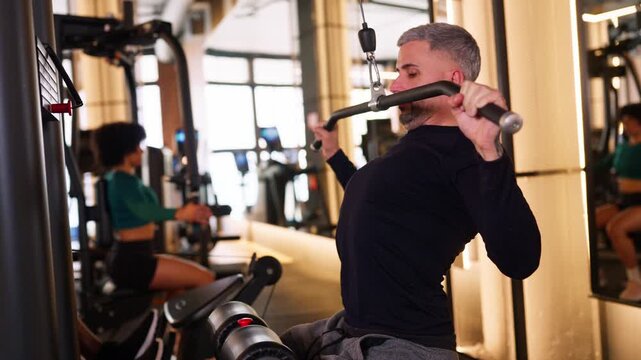 Determined mature man working out on a lat pulldown machine in the gym