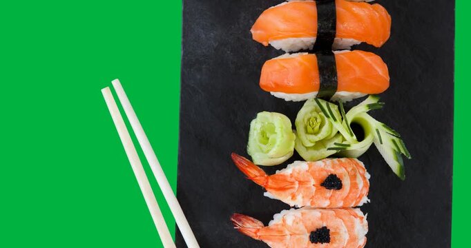 Overhead view of sushi in a plate and chopsticks against black background