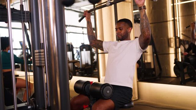 Tattooed muscular man training back on lat pulldown machine