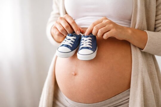 Pregnant woman holding baby shoes on belly expecting motherhood concept
