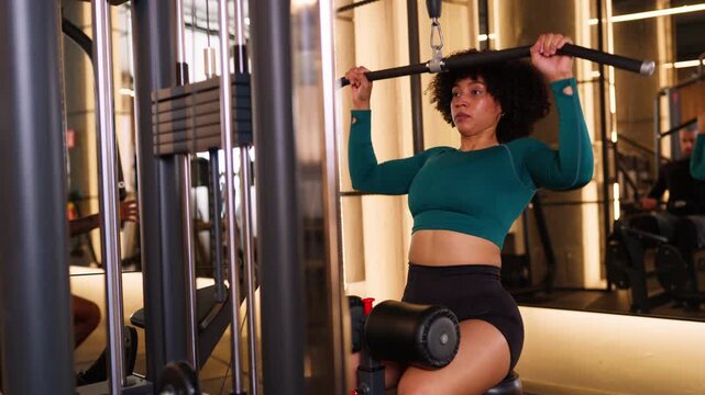Determined woman training back muscles on lat pulldown machine