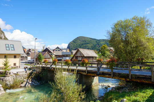 Traditional wooden bridge with red flowers over a crystal clear river in Studor v Bohinju, scenic alpine village in Slovenia near Lake Bohinj, Julian Alps, Triglav National Park