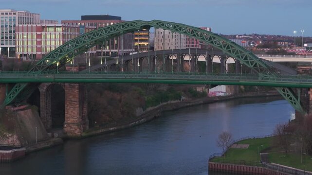 Aerial telephoto tracking shot of the Wearmouth Bridge in Sunderland at dawn, with city lights reflecting on the River Wear.