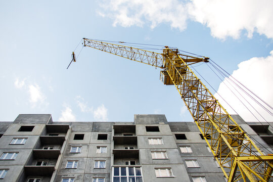 A large yellow tower crane is positioned next to a concrete residential building in the process of construction, with a bright sky overhead