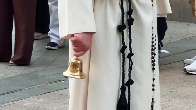 catholic priest white vestment holding golden bell black rosary beads religious procession outdoor ceremony sacred faith traditional clergy spiritual celebration street