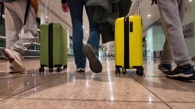 Low-angle view of a family walking with wheeled suitcases and luggage through an airport terminal corridor, ready for departure on a business trip or family vacation