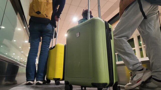 Family with a child and colorful luggage traveling on a moving walkway at the airport, seen from a low angle as they head towards their departure gate for a holiday trip