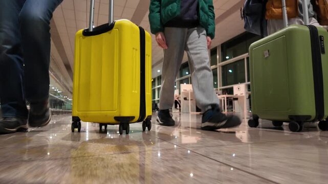 Family walking with colorful suitcases through a modern airport terminal, low-angle view of travelers' feet and luggage moving along the polished floor toward their gate