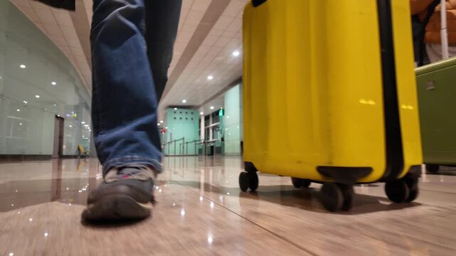 Low angle shot of people with luggage walking through an airport terminal, the camera following a yellow suitcase rolling on the polished floor towards the departure gate
