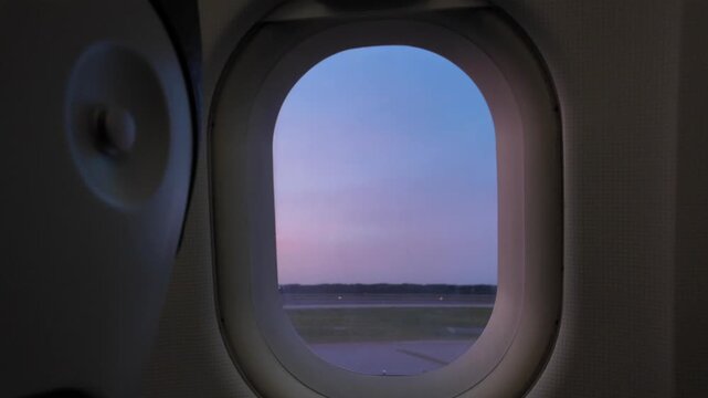 Scenic flight at dawn viewing airplane wing and airport runway from inside the cabin, airplane window view of the sunrise sky and taxiway before takeoff on a commercial jet