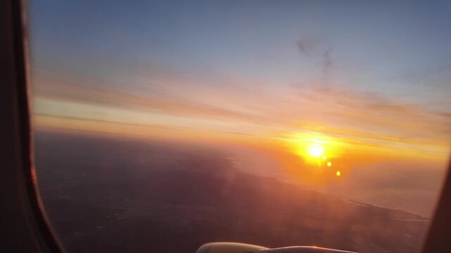 Airplane window view capturing a beautiful golden sunset from the cabin during a flight with the sun disappearing below the horizon creating a serene and dark atmosphere