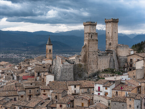 Aerial view of the medieval Caldora Castle and historic stone houses under a dramatic cloudy sky in Pacentro, Abruzzo, Italy.