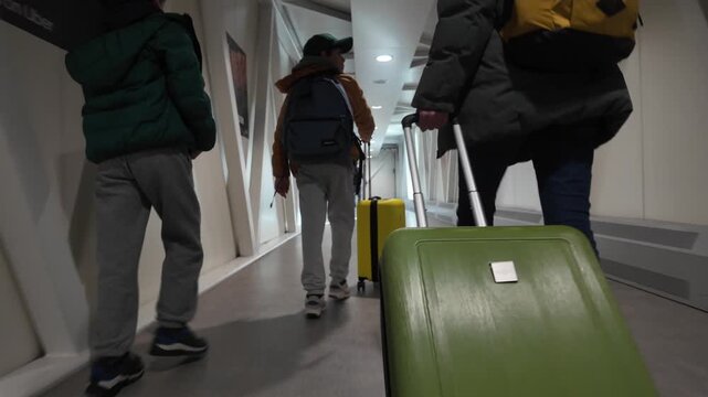 Family walking with luggage at the airport, passengers boarding the plane through the jet bridge, travelers with baggage going on a journey, view from the back
