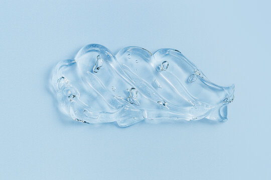 Close up of transparent cosmetic gel swatch with air bubbles on soft blue background. Glossy texture and fluid shape emphasize hydration, moisturizing, purity, and modern skincare aesthetics, top view