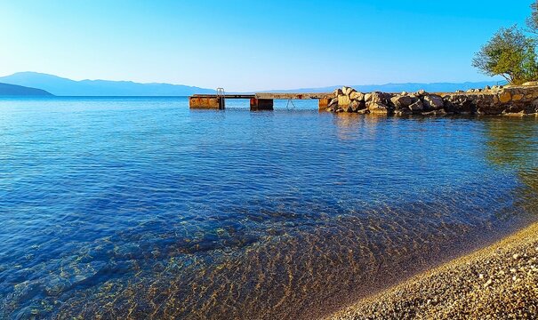 Dock in the sea with big rocks, beach and blue sea horizon, peaceful beach background 