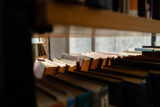 Old books on the bookshelf in library archive interior in sunny day. Shallow depth of field