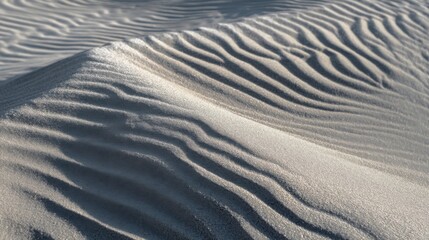 Fototapeta premium Delicate dune surface with wavy patterns, side-lit sunlight creating interwoven shadows on rippled sand.
