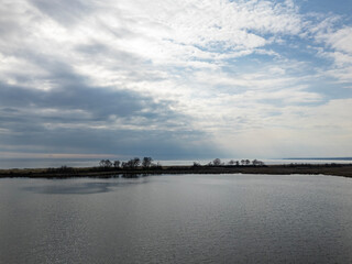 Obraz premium Still Lake Water Reflecting Cloudy Sky Over Island Trees in Demirkoy