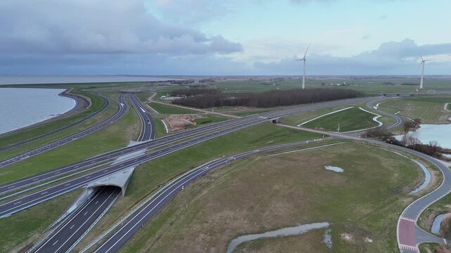 Forward drone flight toward the highway interchange before the Afsluitdijk with tunnel roads and layered transport lines.